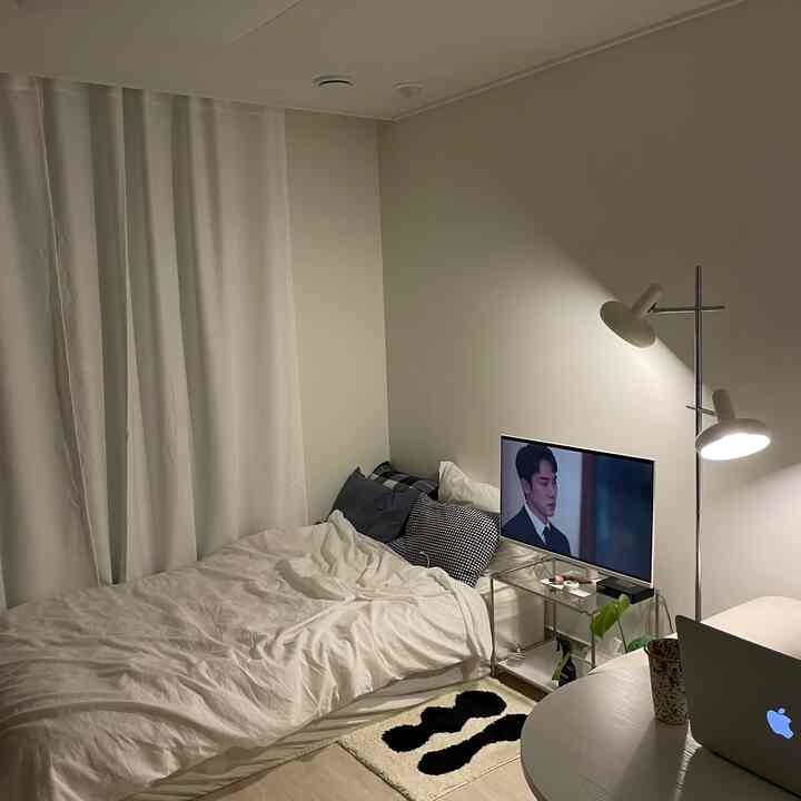 白色トーンの落ち着いた一人暮らし用寝室、ベッドと遮光カーテン、フロアランプが配置された雰囲気のあるインテリア