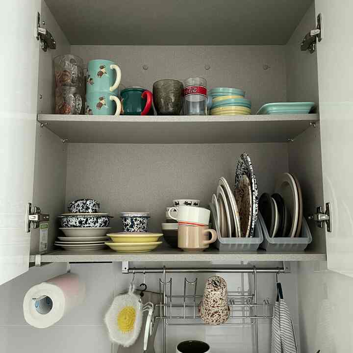 白いキャビネット内に整理された皿とカップがあるコンパクトなキッチン収納スペース