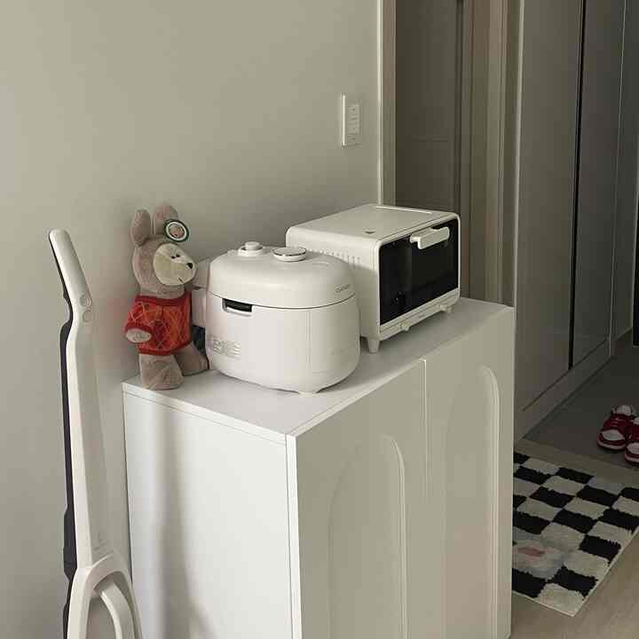 白とナチュラルな色調の狭い玄関スペース、収納棚にミニオーブンと炊飯器が置かれたすっきりとしたインテリア