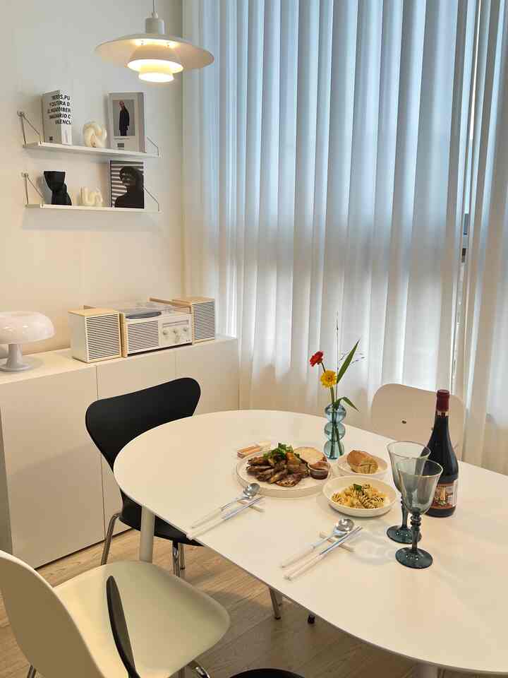 ホワイトとモダンな雰囲気のダイニングルーム、白い楕円形のダイニングテーブル、白黒の椅子、シアーカーテンが配された清潔感のあるインテリア