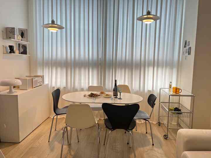 ホワイトとシルバーのトーンのダイニングルーム、白いダイニングテーブルと黒・ベージュの椅子が配置され、柔らかな白いシフォンカーテンが背景にある雰囲気のあるインテリア