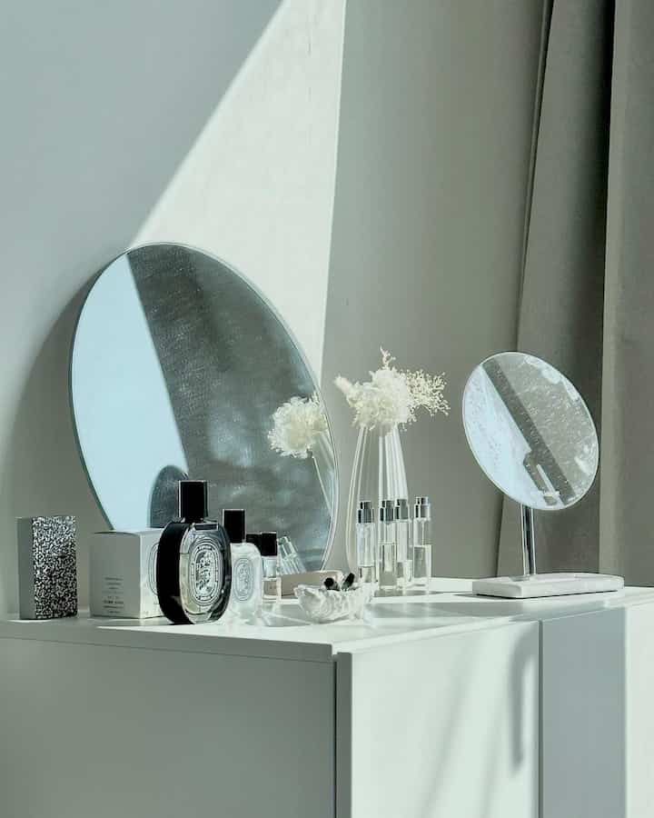 ホワイトトーンのパウダールーム収納の上に丸い化粧台ミラーと化粧品、ドライフラワーが配置されたミニマルなインテリア