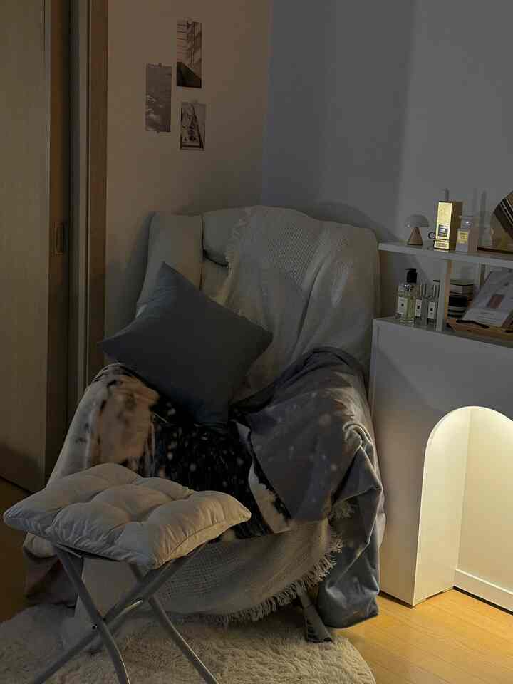 ウッド調の床と白いコンソールがある、クッションとブランケットが配置された居心地の良い一人暮らし向けの空間。