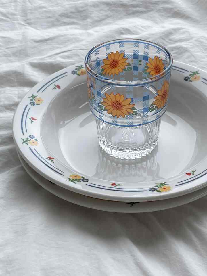 白い背景に花柄の皿とひまわり模様のガラスが置かれたかわいいレトロスタイルの食器