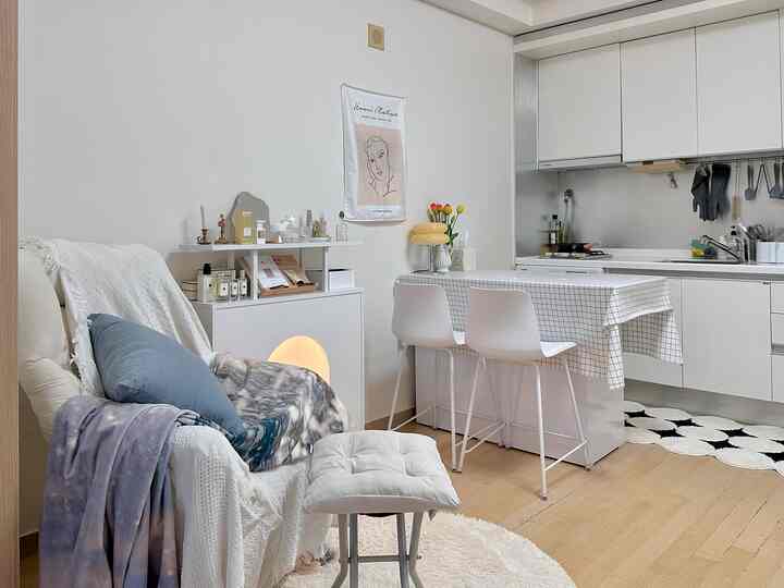 ホワイトとナチュラルトーンのワンルームキッチンダイニングスペース、居心地の良いアームチェアとチェック柄テーブルクロスが配置された印象的なホームカフェインテリア