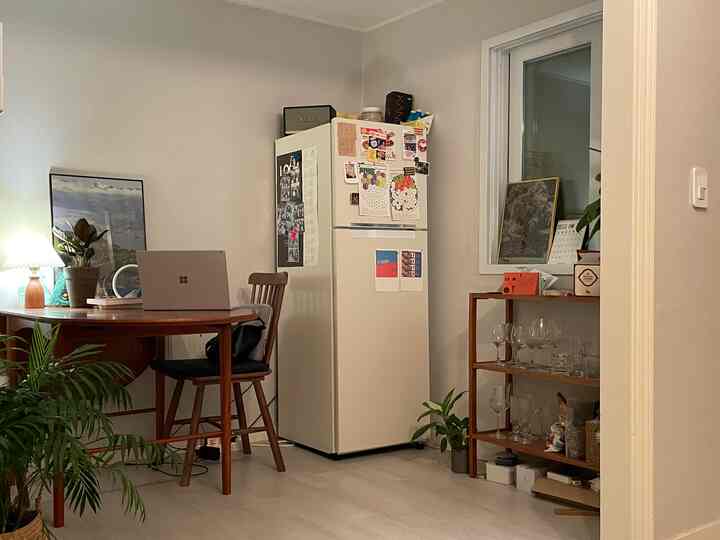 白を基調とした木目調の家具が配置された狭いキッチンダイニング、レトロなステッカーが貼られた冷蔵庫と収納棚がある雰囲気のあるインテリア