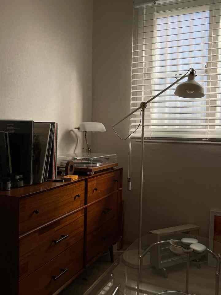 ホワイトトーンと木目調が調和した寝室、木製チェストの上にターンテーブルとデスクランプが配置された落ち着いたインテリア