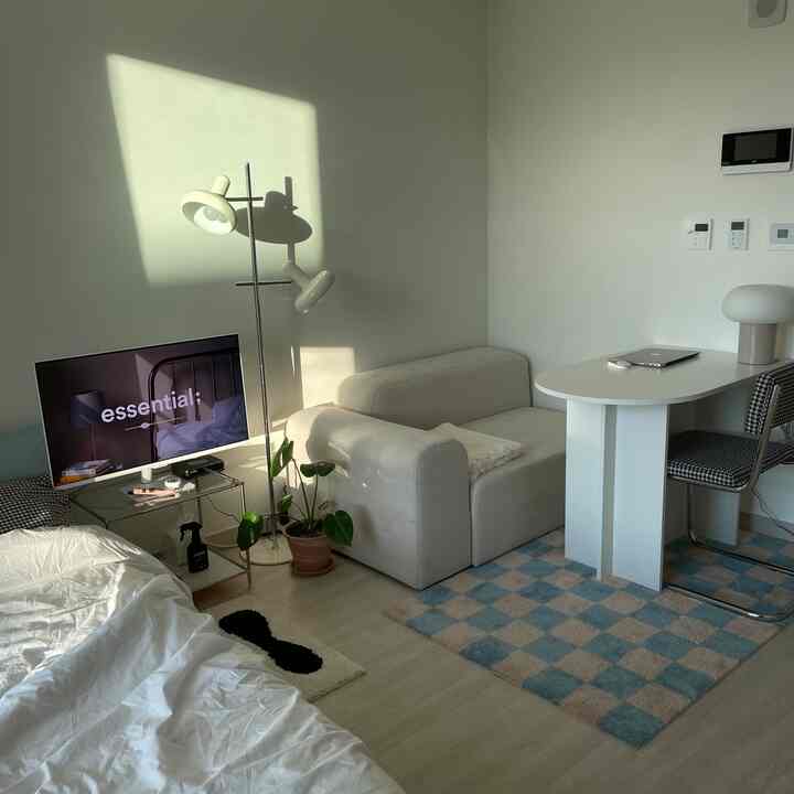 ホワイトとベージュの色調のリビング、アイボリーのソファとチェック柄のラグ、ノートパソコンのあるテーブルが配置された落ち着いた雰囲気のインテリア