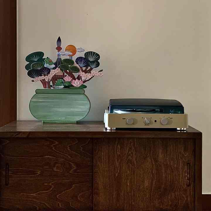 ブラウンの木製キャビネットの上にレトロなターンテーブルと小物が置かれた、ナチュラルな雰囲気の落ち着いた空間