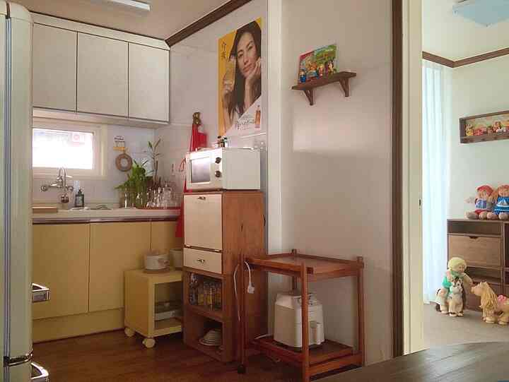 バター色のキッチンと木製家具が配された温かみのある空間、隣に子供のおもちゃや人形が置かれた小さな部屋が見える印象的なインテリア