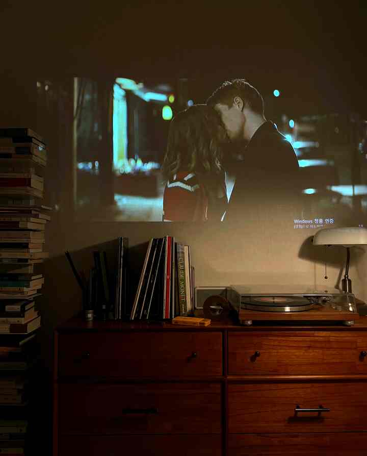 暖かい木目調の狭い部屋、ヴィンテージのターンテーブルとナイトテーブル、そして映画が投影されたプロジェクターによる雰囲気のあるホームシネマ空間
