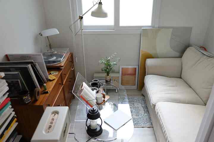 ナチュラルな色調の狭いリビング、ベージュのソファと透明なガラスのコーヒーテーブル、木製の収納家具とフロアランプが配置された雰囲気のあるインテリア