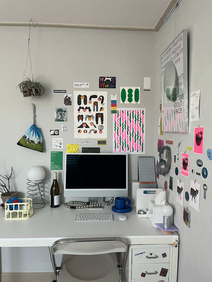 ホワイトトーンのコンパクトなホームオフィス、iMacと清潔なデスク、多彩なウォールアートが配置された印象的な作業空間