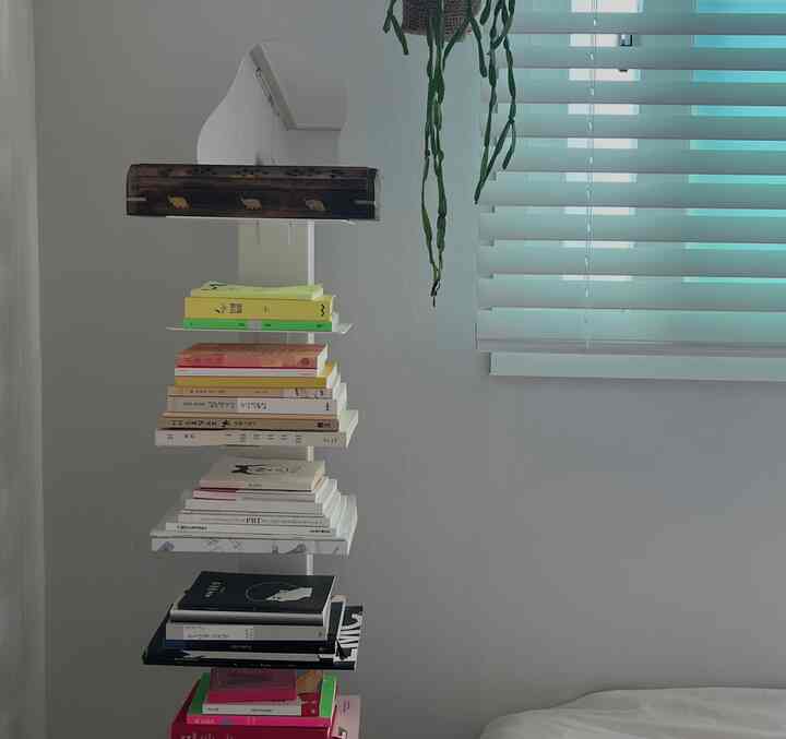 ナチュラルな色調の寝室、壁に設置された白い本棚タワーとウッドブラインドが調和するシンプルなインテリア