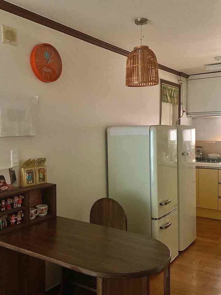 ナチュラルウッドトーンとクリーム色の家電が調和する温かみのあるキッチン、レトロな冷蔵庫とダイニングテーブルが配置された印象的な空間