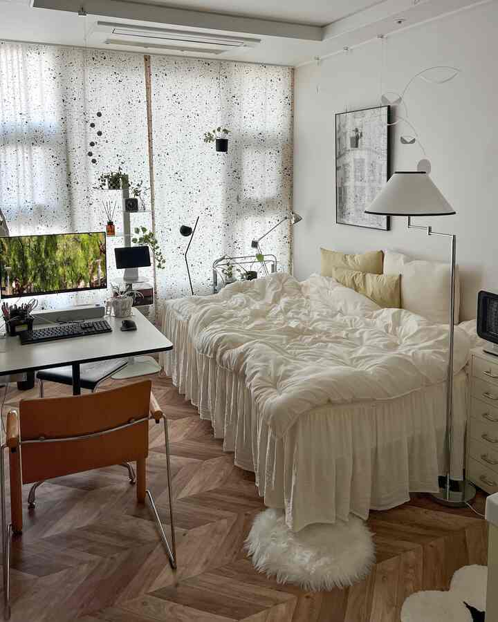 ホワイトとベージュのトーンのワンルーム寝室、ベッドとデスク、植物が配置された落ち着いたナチュラルなインテリア