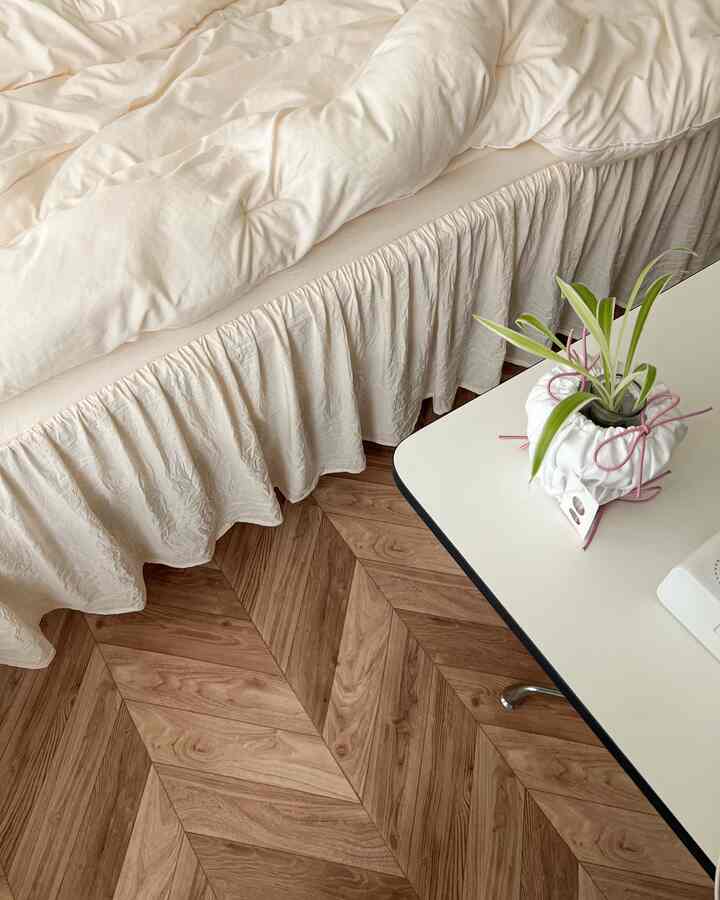 ベージュのベッドスカートとヘリンボーン木目調のセルフ貼るだけ床シートが敷かれたナチュラルなワンルーム寝室のインテリア