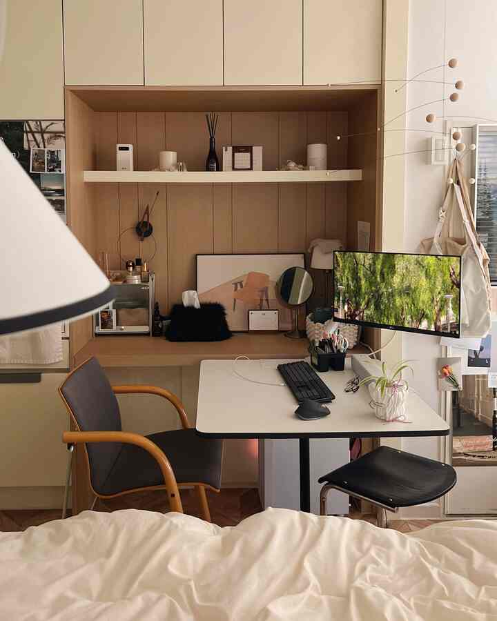 ナチュラルなベージュと木目調のワンルーム寝室兼ホームオフィス、木製椅子と白いデスクにモニターとキーボードが配置された落ち着いた空間