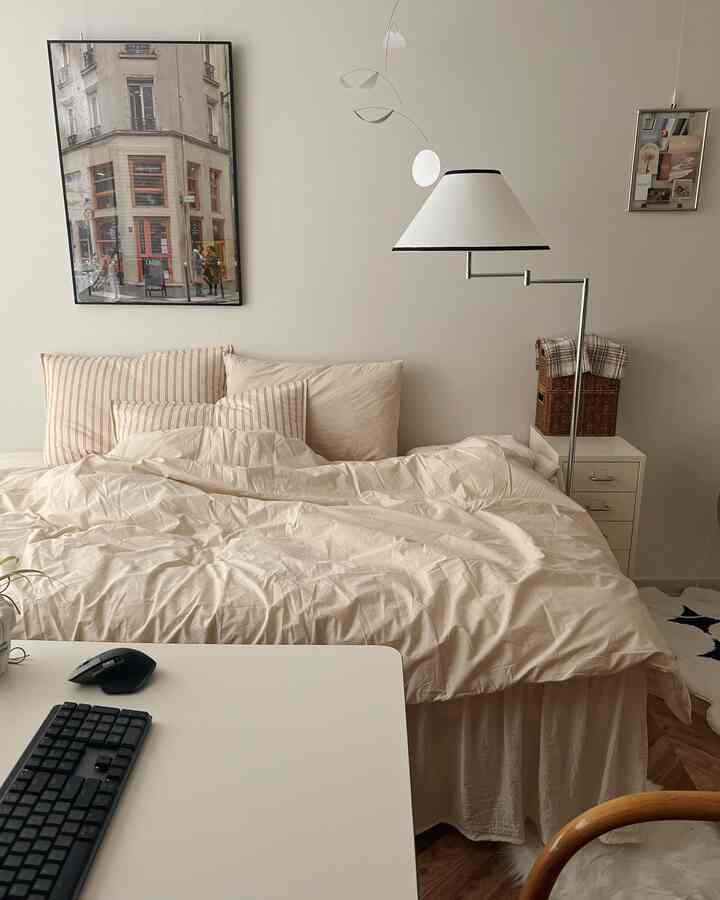 アイボリーとベージュのトーンの寝室、快適な寝具とフロアランプ、デスクと木目調の椅子が調和した雰囲気のあるインテリア