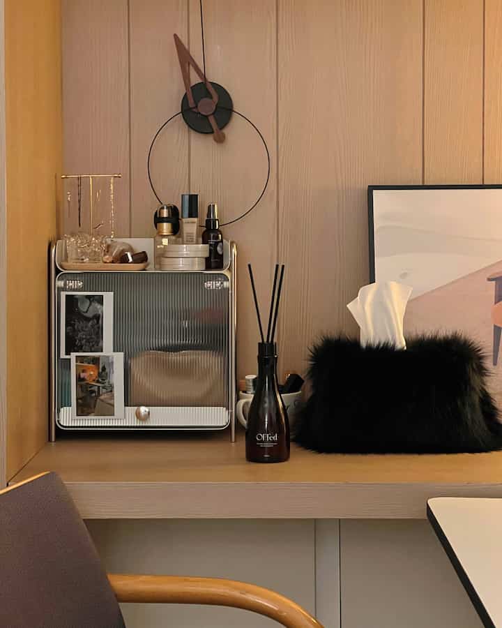 ベージュとウッドトーンの化粧台空間、壁時計やディフューザー、ポスターが配置された落ち着いた清潔感のあるインテリア
