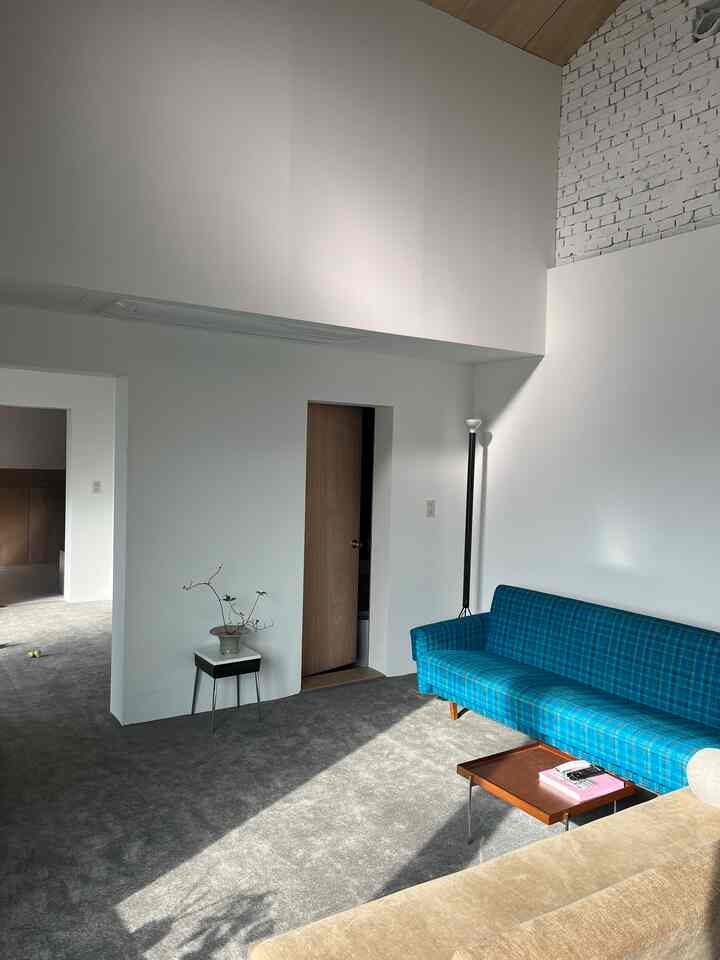 グレーのロールカーペットの床とブルーチェックのソファが配置されたリビング、明るく開放的な雰囲気のインテリア