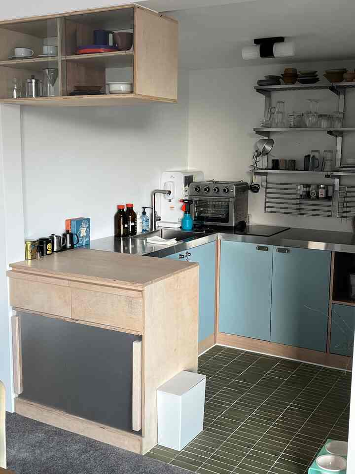 白い壁と緑のタイル床が印象的なナチュラルトーンのキッチンスペース、ステンレス棚と整った収納が調和した雰囲気のあるインテリア