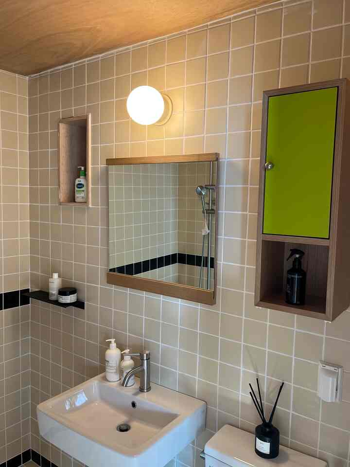 ベージュのタイル壁と木目調の収納がある、丸い壁灯と鏡が印象的な清潔感のあるバスルーム