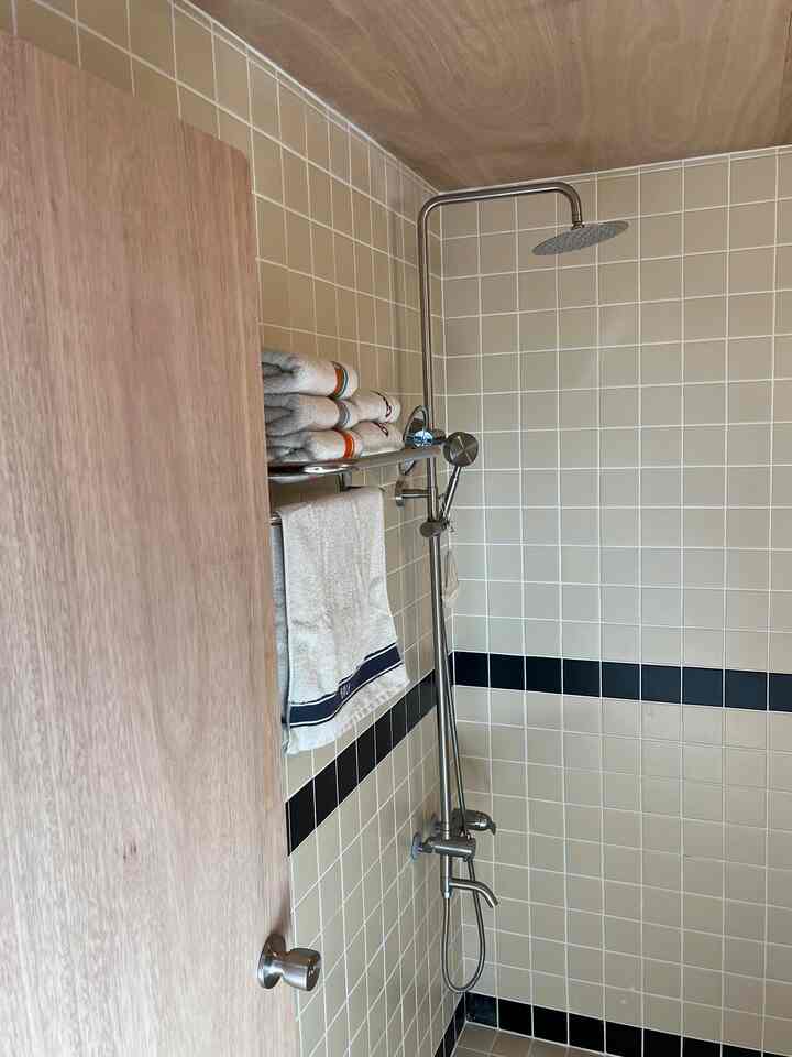 ベージュと黒のタイル壁のあるバスルーム、シャワーとタオルラックが配置されたヴィンテージモダンな空間