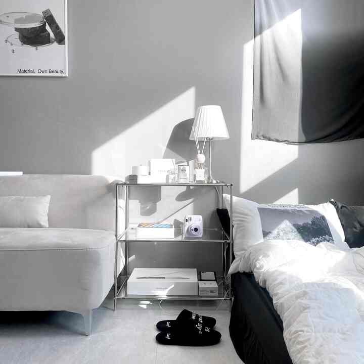 モノトーンのワンルーム空間、グレーのソファと白いベッド、ナイトテーブルのランプとディフューザーが配置されたシンプルでモダンなインテリア