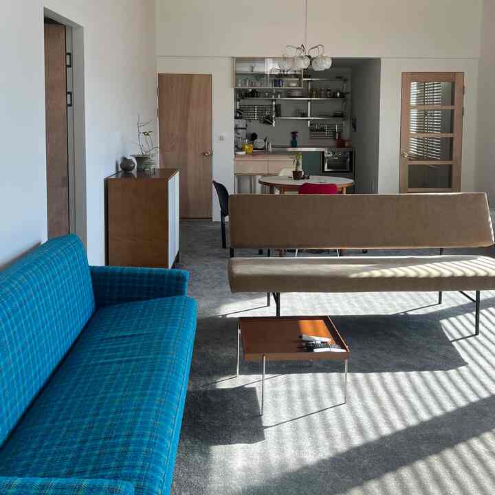 ブルーのソファとベージュのソファベンチが配置された縦長のリビング、木製家具とグレーのカーペットが自然な雰囲気を演出する空間