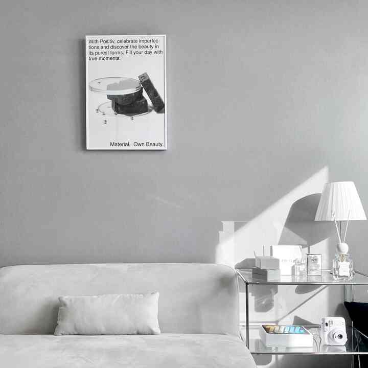 モノトーンのリビング、ライトグレーのソファと透明なシルバーのサイドテーブル、白いランプが配置された清潔でモダンなインテリア