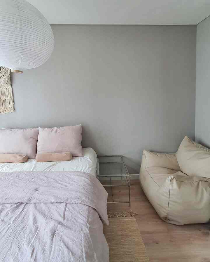 グレーの壁紙とライトブラウンの木製床が特徴の2人用寝室、ピンクの寝具とベージュのビーズクッションが配置されたモダンで自然な雰囲気のインテリア