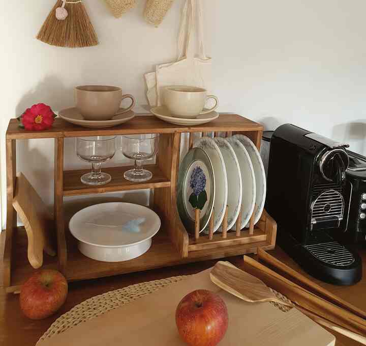 白い壁と木目調の木製棚がある、コーヒーマシンや皿、カップが配置された落ち着いたキッチンのおうちカフェ空間