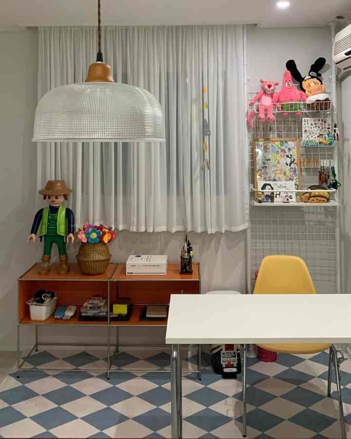 白と黄色のトーンの書斎兼趣味部屋、シンプルなデスクとペンダントライト、玩具や小物が配置された印象的な空間