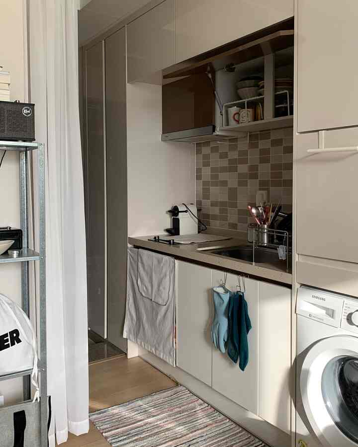 明るいホワイトとナチュラルウッドトーンが調和する狭小な一人暮らし用キッチン、拡張型食器ラックと洗濯機を備えた実用的な空間