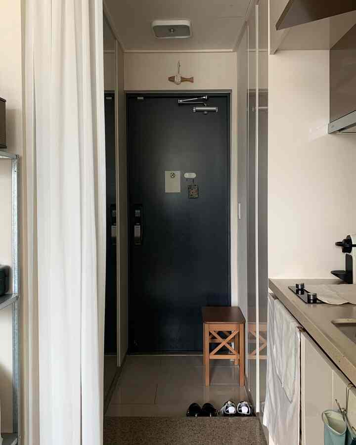 ホワイトとブラウン調の狭い玄関、木製スツールと整然とした収納アイテムが配置された実用的な空間