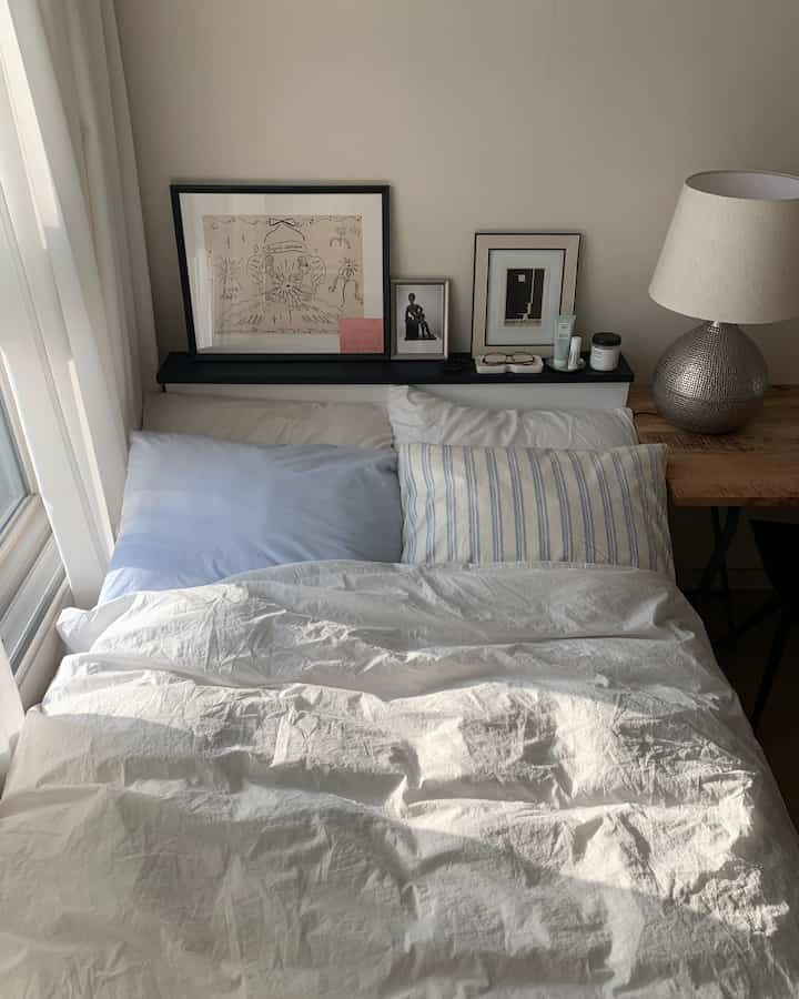 白を基調とした寝室、淡い青のアクセント枕、ベッドとヴィンテージのテーブルランプが調和した印象的な空間