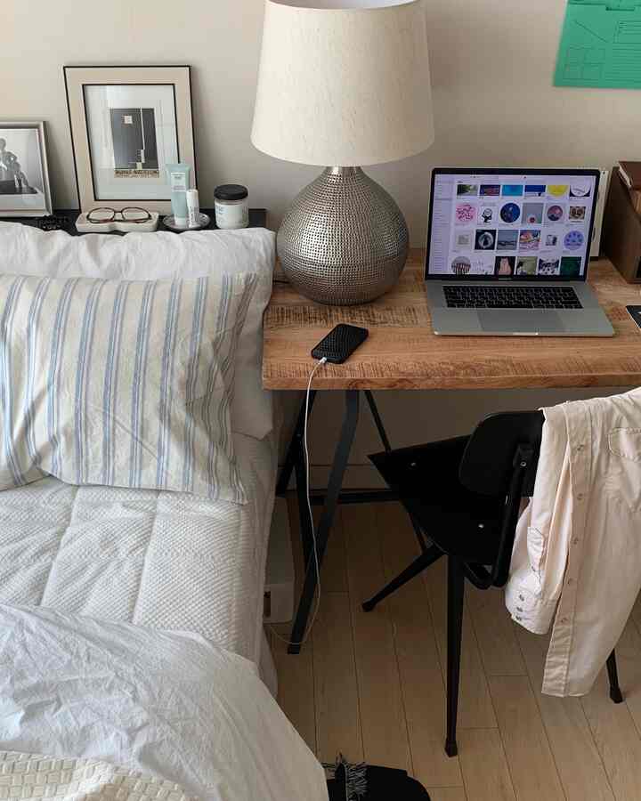 ホワイトとウッドトーンの調和がとれたワンルームの寝室兼ホームオフィス、ベッドと木製デスクにランプが配置された雰囲気のあるインテリア