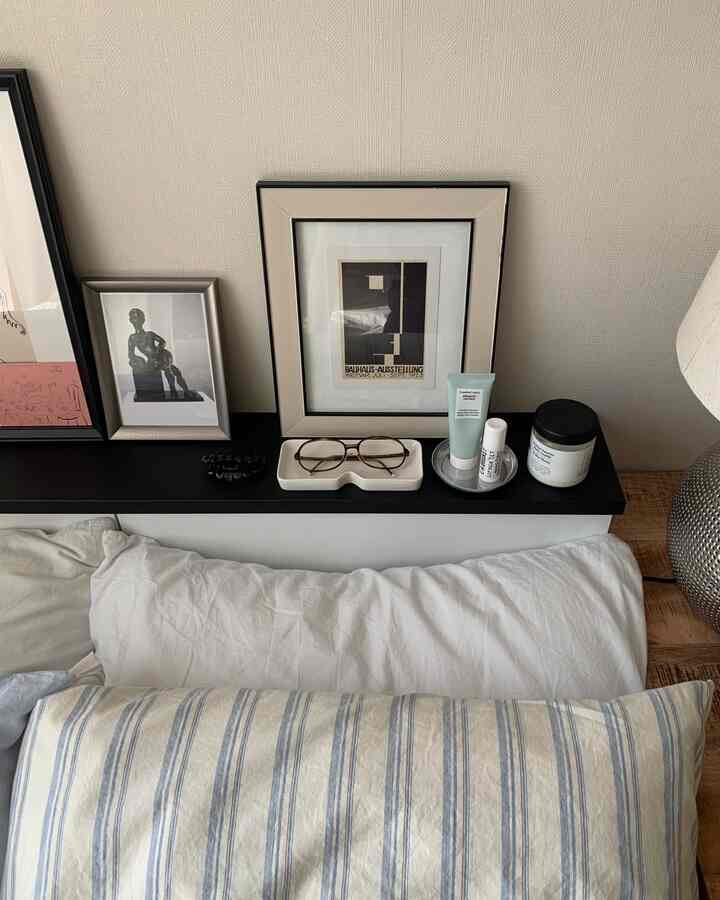 ホワイトと木目調が調和した寝室の棚に眼鏡トレイ、スキンケア用品、額縁が配置されたシンプルモダンなインテリア