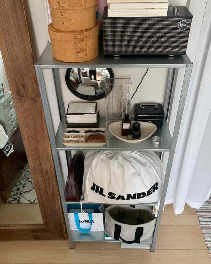 ホワイトとナチュラルカラーの玄関、メタルシェルフと丸い鏡、多様な小物が整然と収納された実用的なスペース