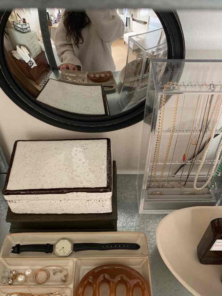 透明なアクリルのネックレス収納とブラウンのアクセサリー、黒い丸い鏡が置かれたすっきりとしたドレッサーの上の空間