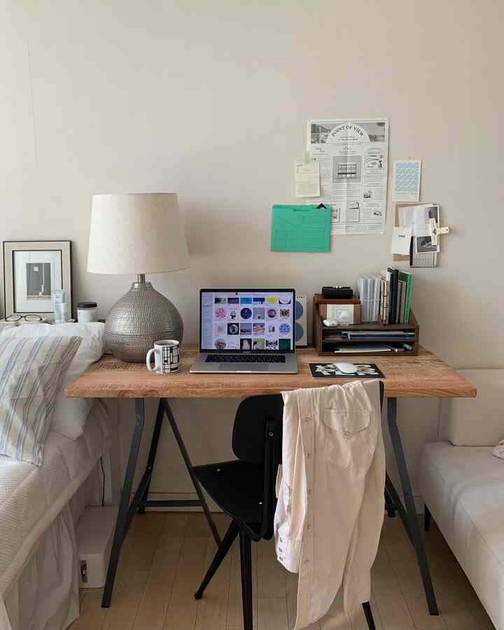 白い壁と木目調のデスクがあるワンルームのホームオフィス、ノートパソコンとテーブルランプが置かれた整った作業空間