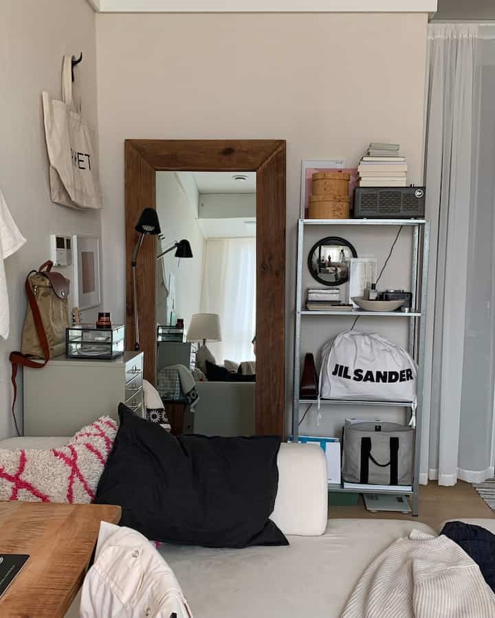 ホワイトとブラウンのトーンの狭いリビング、木製の大きな全身鏡とメタルシェルフ、ホワイトソファが配置された抜け感のあるインテリア