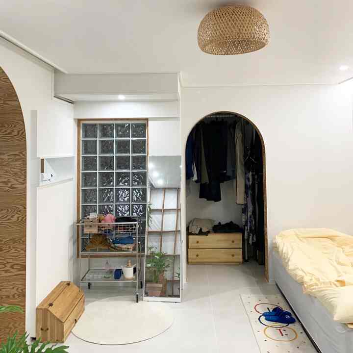 白と木目調が調和したワンルームの寝室、アーチ型のクローゼットと収納棚が配置された整った空間