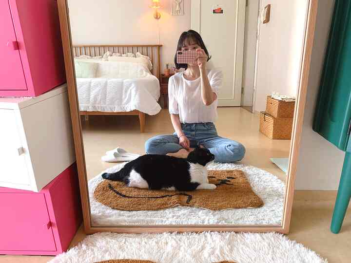 ナチュラルな色調の寝室、全身鏡とラグの上に座る猫がいる印象的な空間