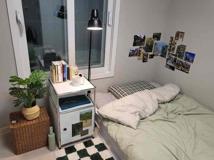 ホワイトとグリーンのトーンの寝室、窓辺の白いナイトテーブルと黒いフロアランプ、壁の写真ギャラリーが温かみのある雰囲気を演出