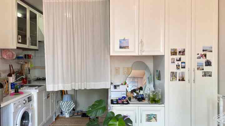 明るくナチュラルカラーの寝室とキッチンがコットンの間仕切りカーテンで分けられた居心地の良いコンパクトな空間