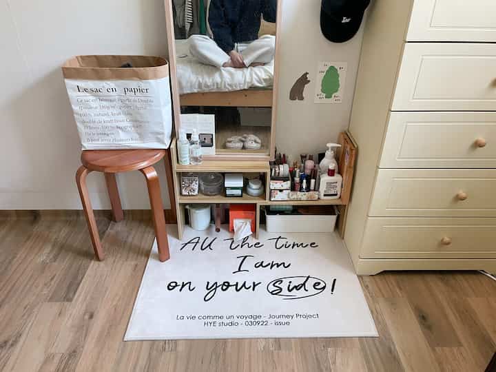 ナチュラルな木目調が特徴的な寝室の一角に配置された化粧台と全身鏡、木製スツールと白いラグがあるコンパクトな空間