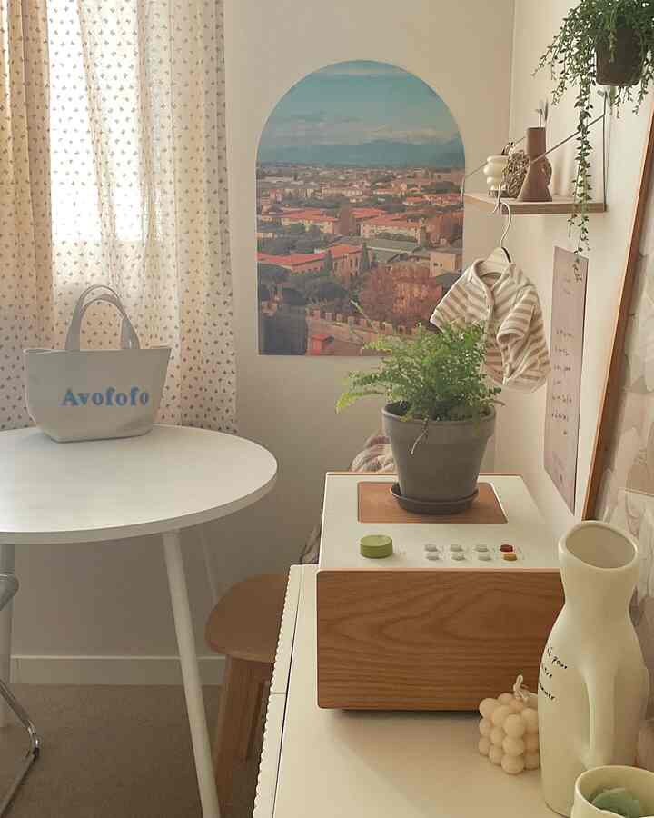 ホワイトと木目調が調和した小さなダイニング、丸い食卓とポスター、植物が温かみのある雰囲気を演出する空間