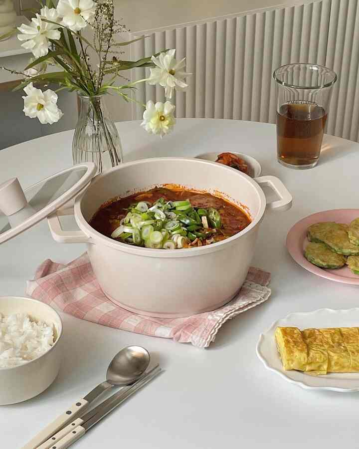白い円形のダイニングテーブルにピンクのチェック柄クロスと鍋、ご飯茶碗、惣菜がきれいに配置されたキッチンスペース